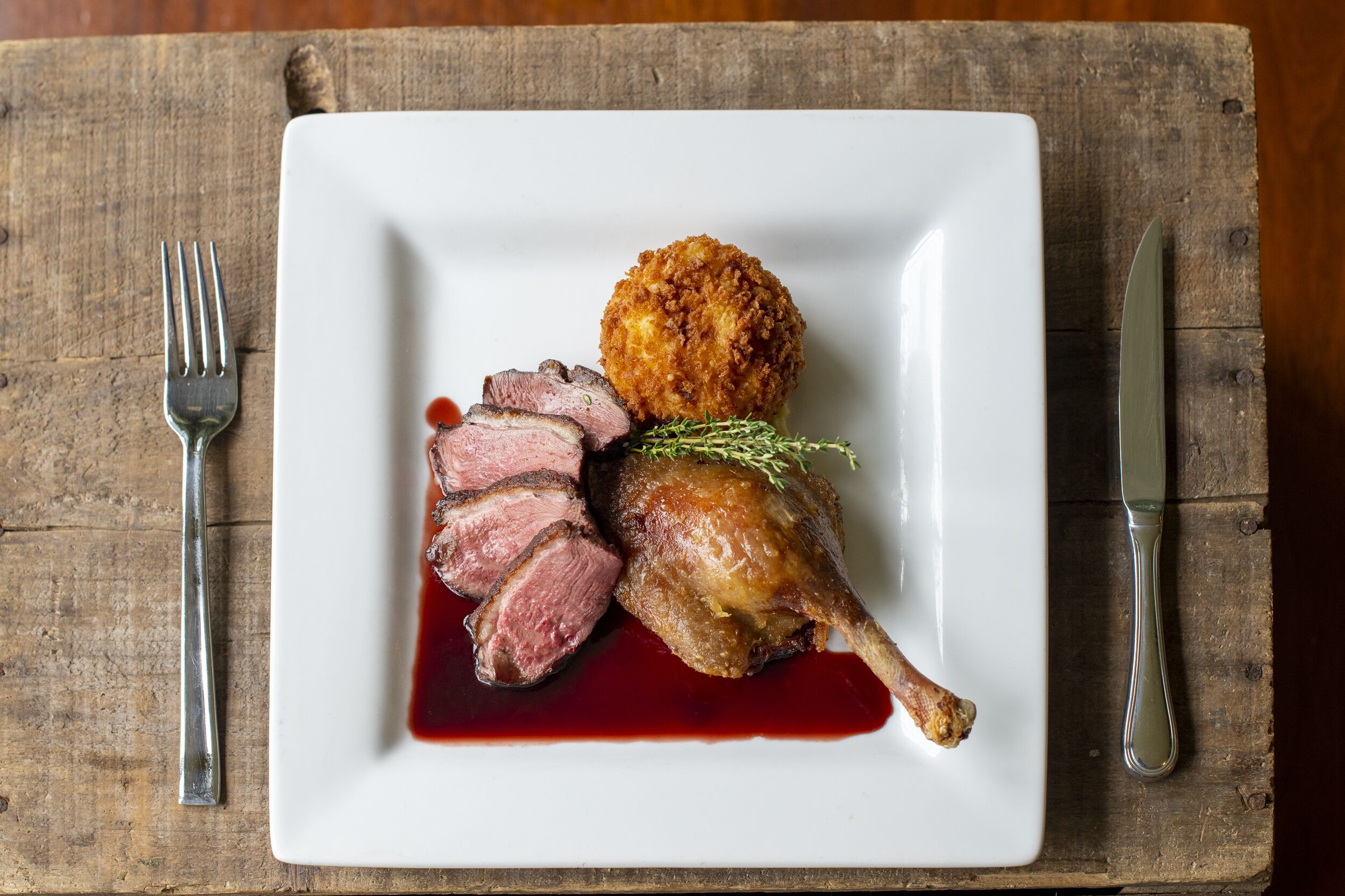 Un plato con pato en rodajas, un alimento empanizado y una guarnición sobre un plato blanco.