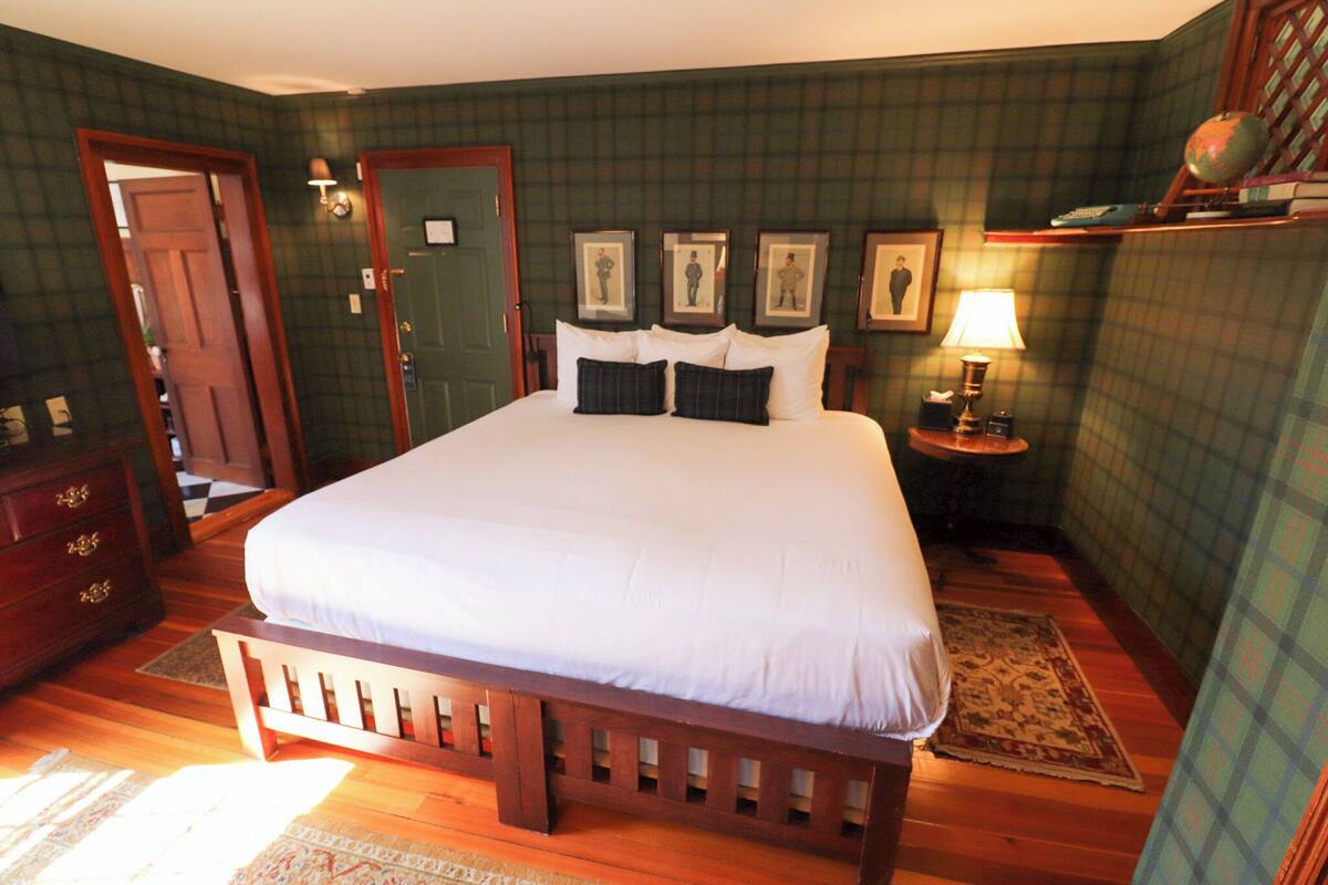 Quarto bem arrumado com uma cama grande, cômoda de madeira, mesa de cabeceira com abajur e quadros nas paredes.