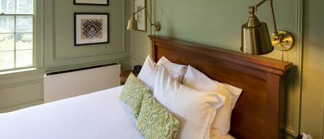 A neatly made bed with white and green pillows, a wooden headboard, and a brass desk lamp on a bedside table.