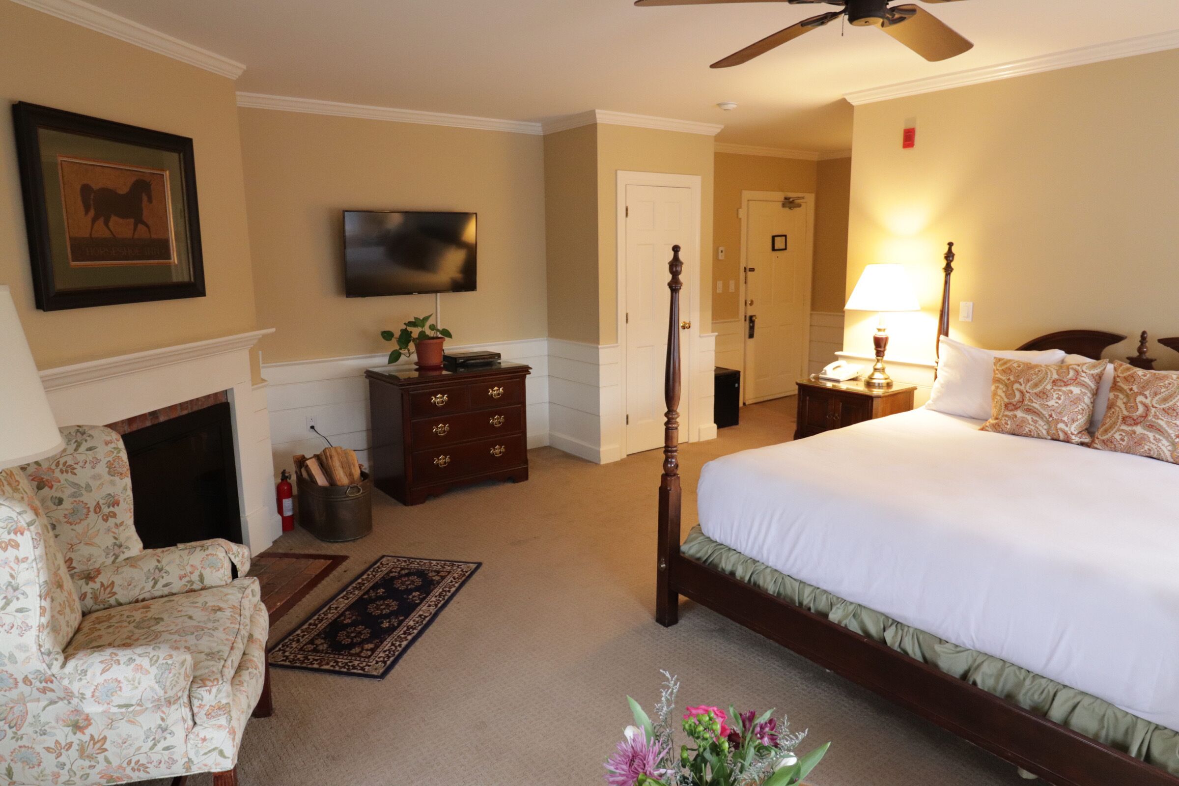 A hotel room with a bed, a chair, a fireplace, a television, and a ceiling fan.