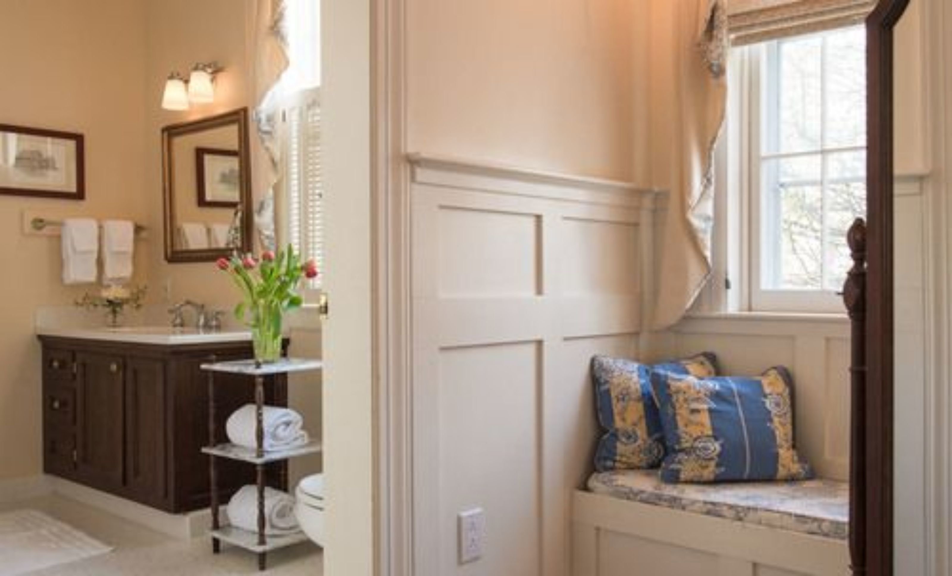 A bathroom with a vanity, a toilet, and a window seat with pillows.