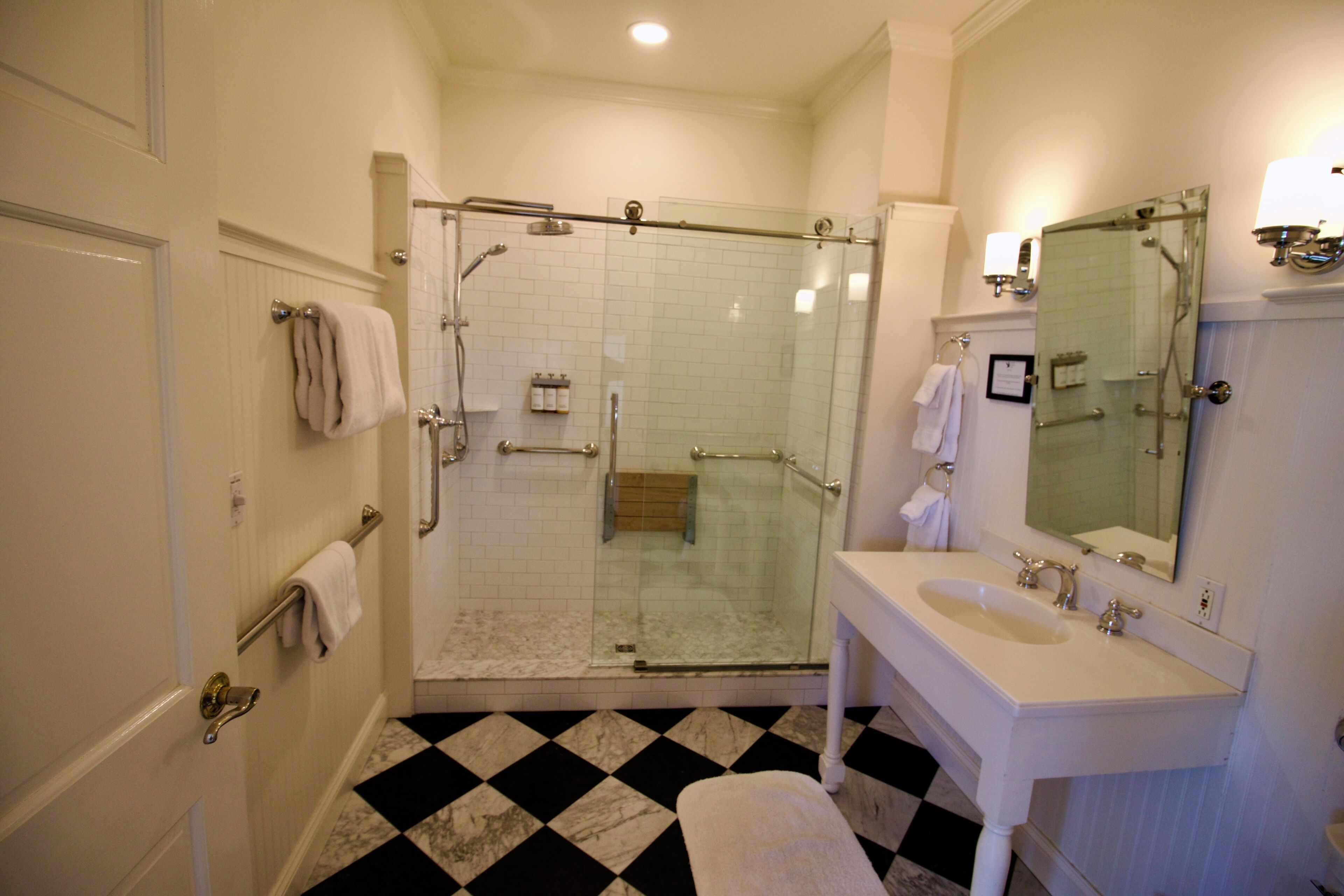 A bathroom with a glass-enclosed shower, a white sink with a mirror, and a checkered floor pattern.
