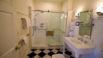 A bathroom with a glass-enclosed shower, a white sink with a mirror, and a checkered floor pattern.