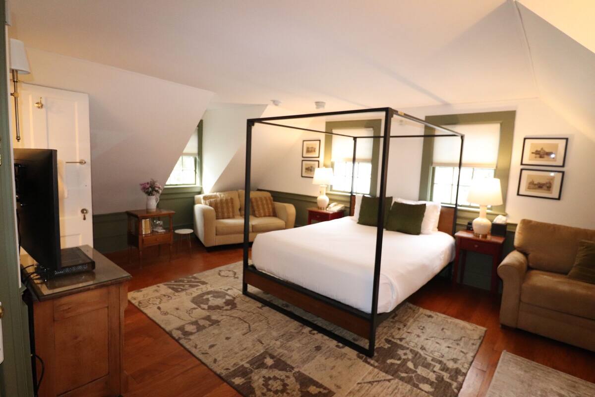 Uma cama com dossel em um quarto com televisão, um sofá e uma escrivaninha.