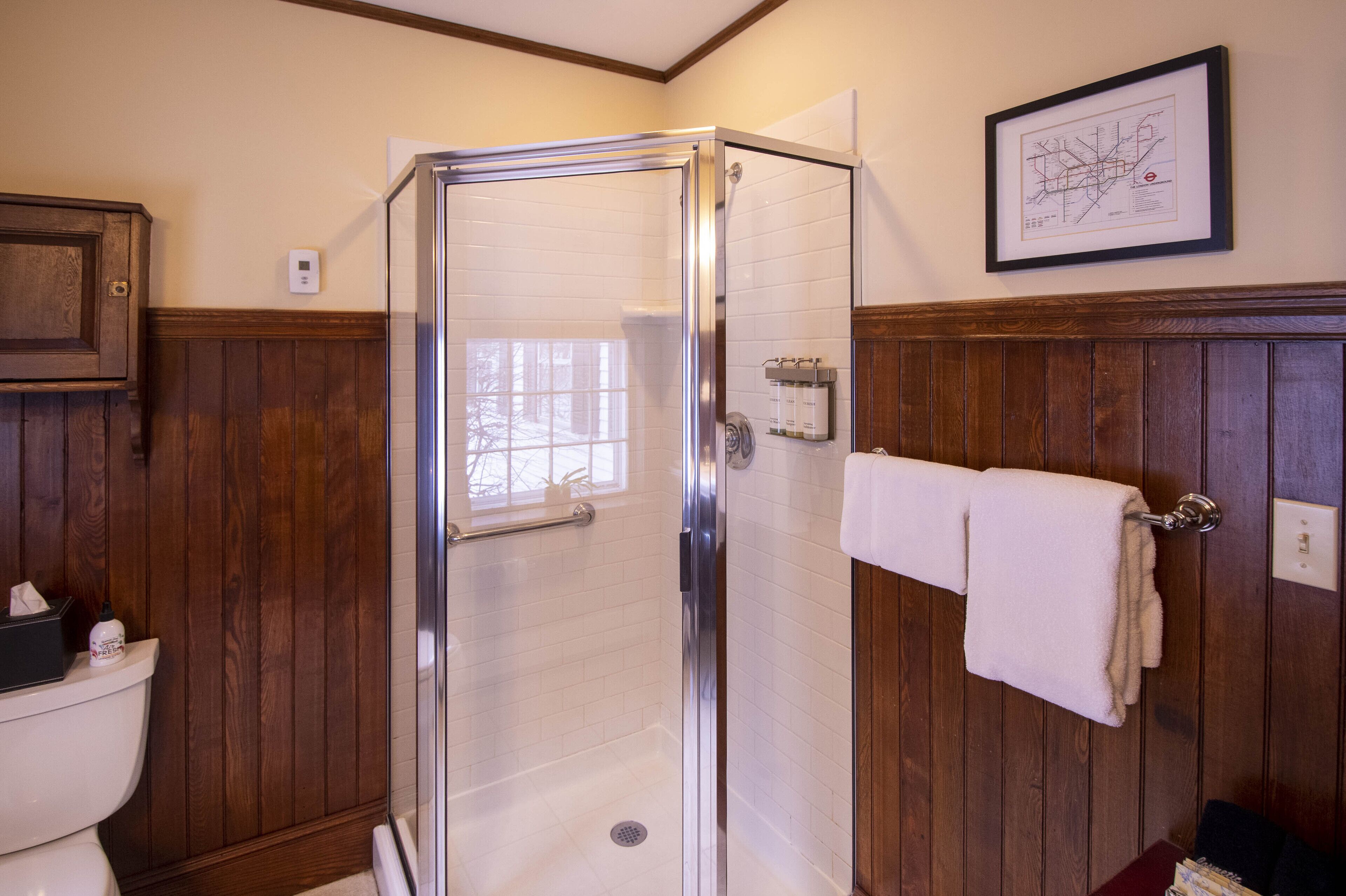 Une salle de bain avec une douche à parois de verre, un lambris en bois, des toilettes blanches et une carte encadrée accrochée au mur.