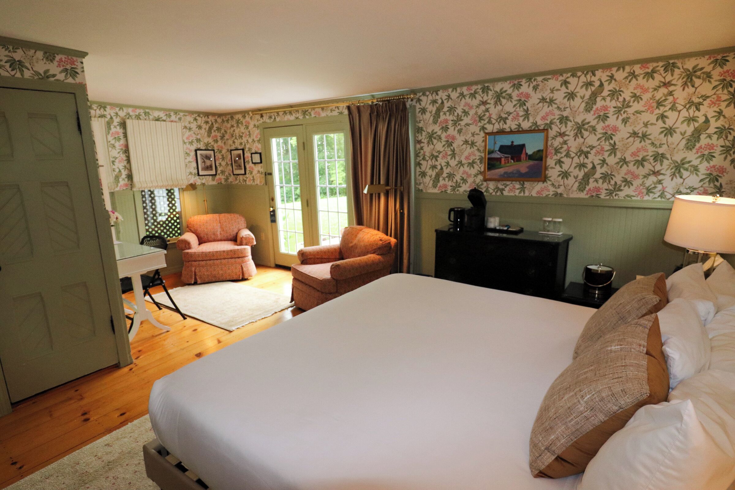 A bedroom with a large bed, two armchairs, a dresser, and a desk with a lamp.