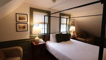 A four-poster bed with white linens, two bedside lamps, a telephone, and framed pictures on the wall.