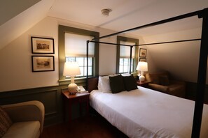 A four-poster bed with white linens, two bedside lamps, a telephone, and framed pictures on the wall.