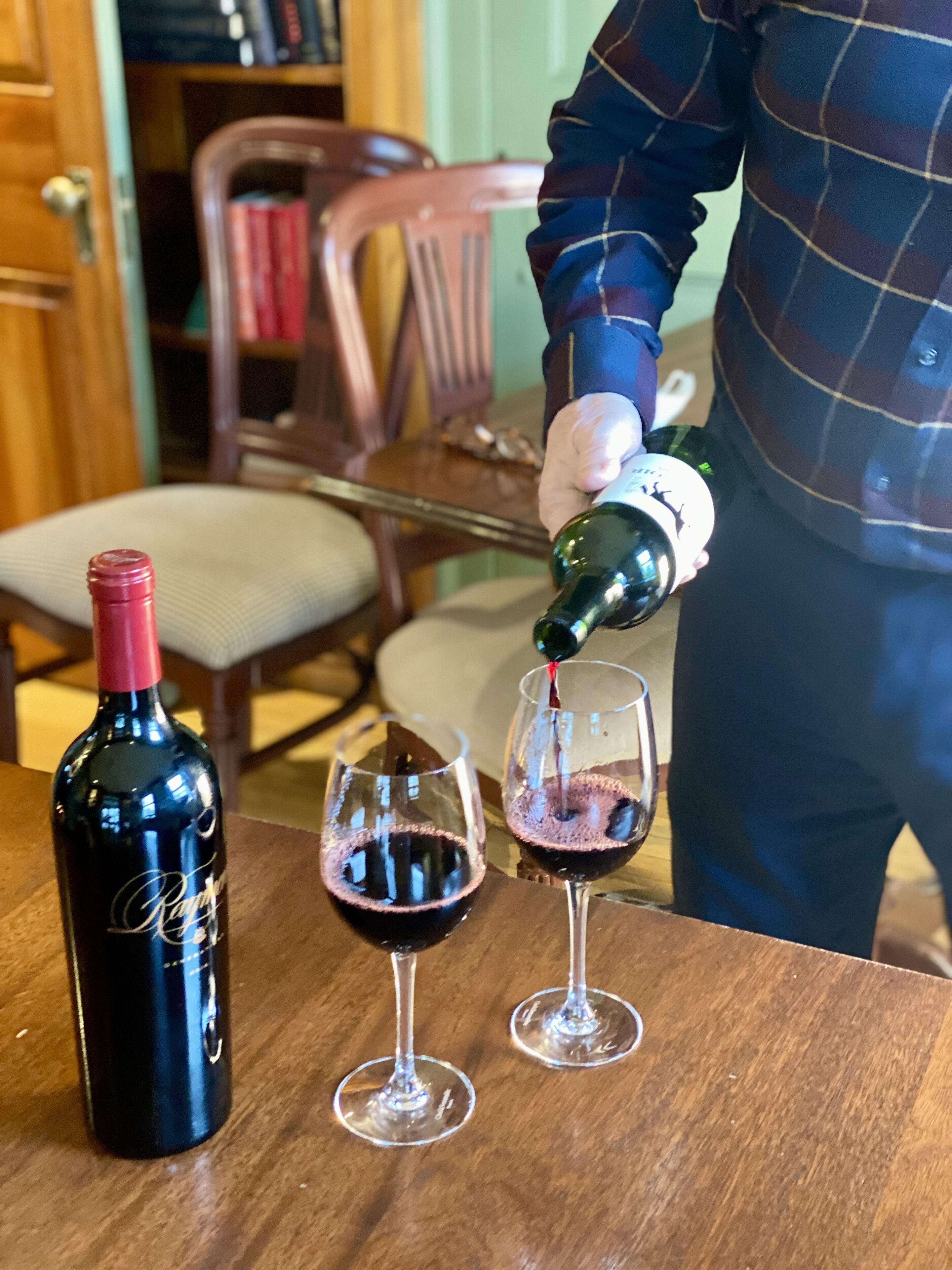 A person pouring wine into two glasses from a bottle on a wooden table.