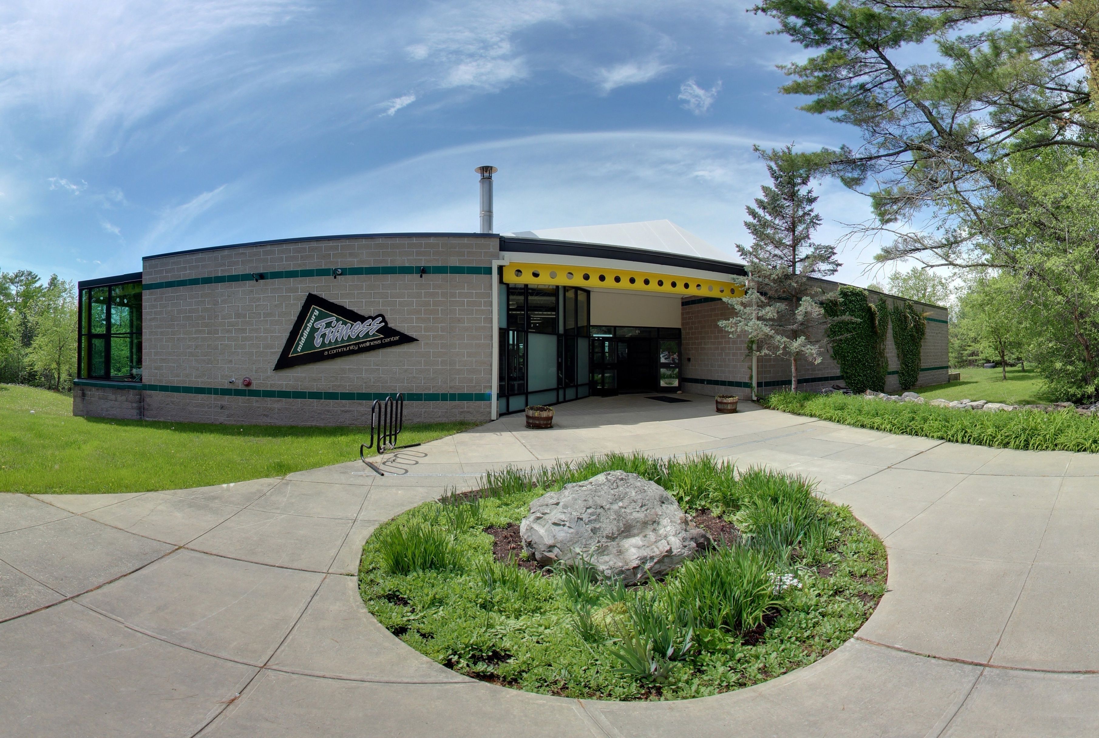 A modern building with a brick facade, large windows, and a circular landscaped area with a rock centerpiece.