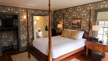 A four-poster bed with a wooden frame, a television, a bedside table with a lamp, and a painting on the wall.
