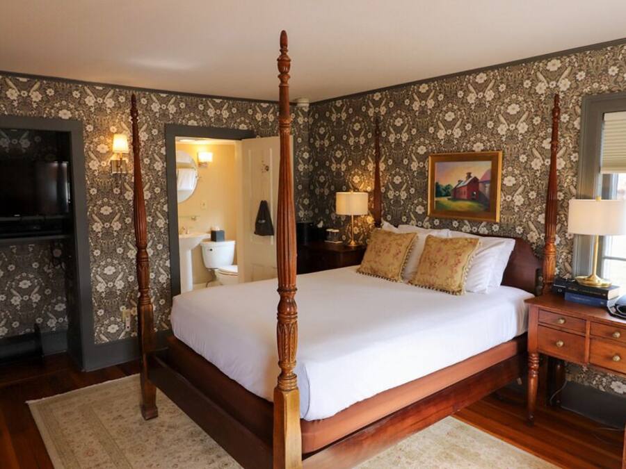 A four-poster bed with a wooden frame, a television, a bedside table with a lamp, and a painting on the wall.