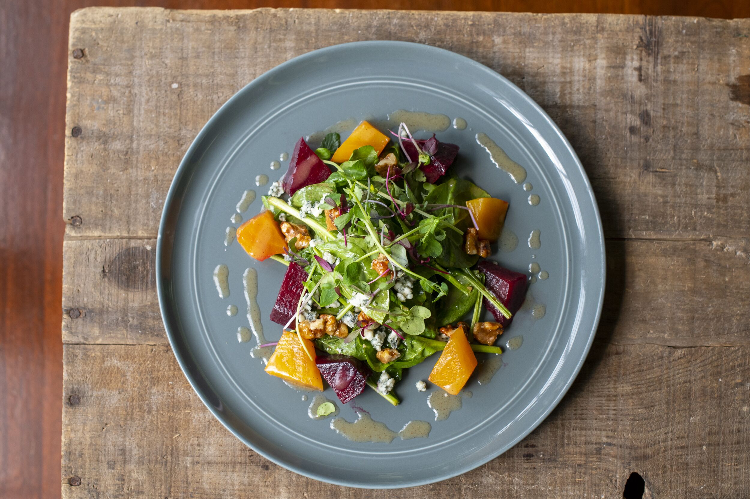 A plate of salad with various vegetables and nuts on a wooden table.