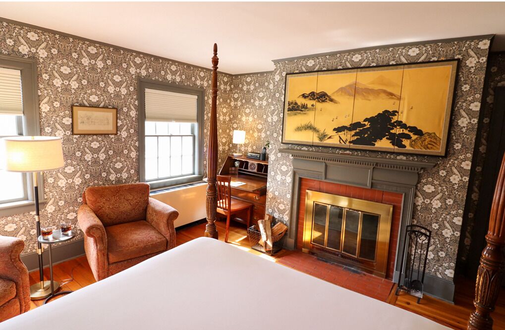 A hotel room with a large bed, a fireplace, a desk with a chair, and a large painting on the wall.