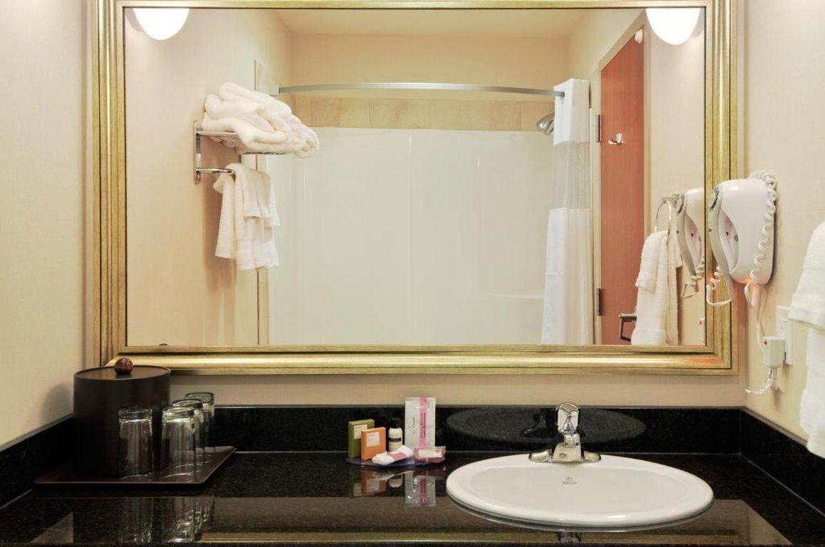 Une salle de bain d’hôtel avec un grand miroir, un lavabo et un porte-serviettes.