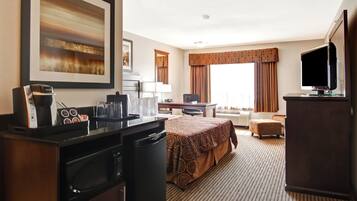 Una habitación de hotel con cama, escritorio, televisión, microondas y cafetera.