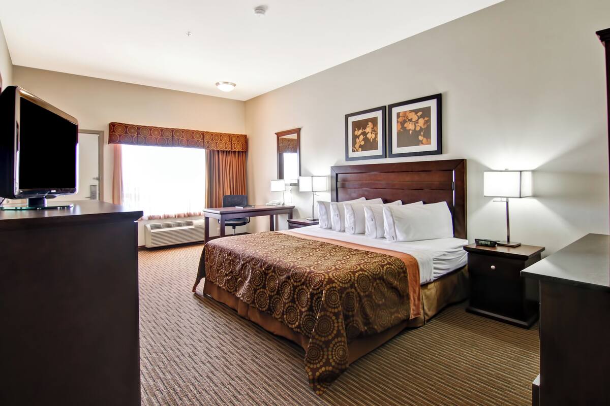 A hotel room with a large bed, a desk with a computer, a TV, and two bedside lamps.