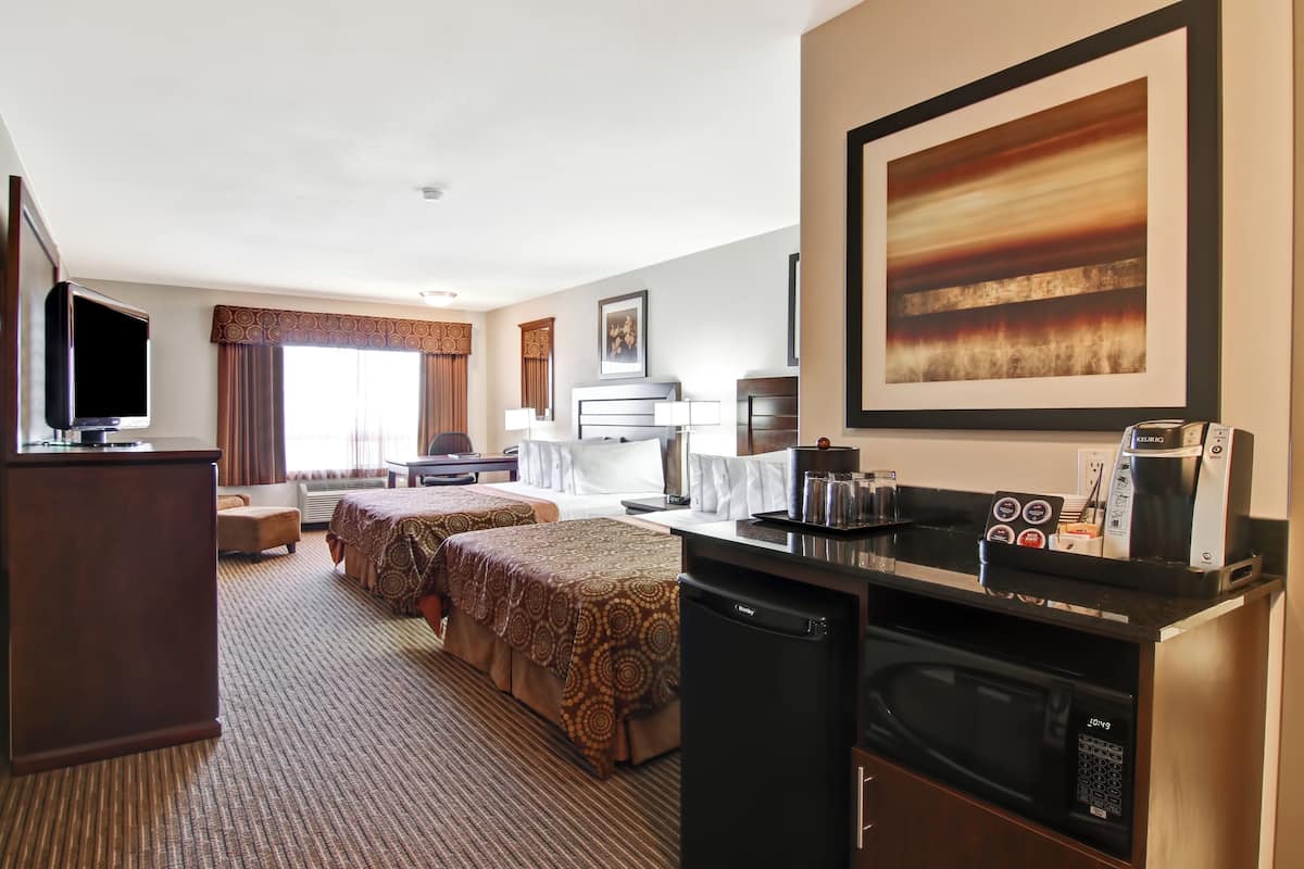 A hotel room with two beds, a television, a kitchenette, and a large framed picture on the wall.