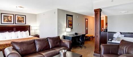 Una habitación de hotel con una cama tamaño king, un sofá de cuero marrón, un escritorio con una silla, y una mesita con una jarra.