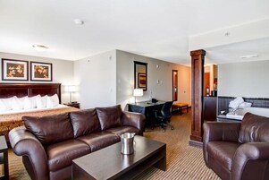 Una habitación de hotel con una cama tamaño king, un sofá de cuero marrón, un escritorio con una silla, y una mesita con una jarra.