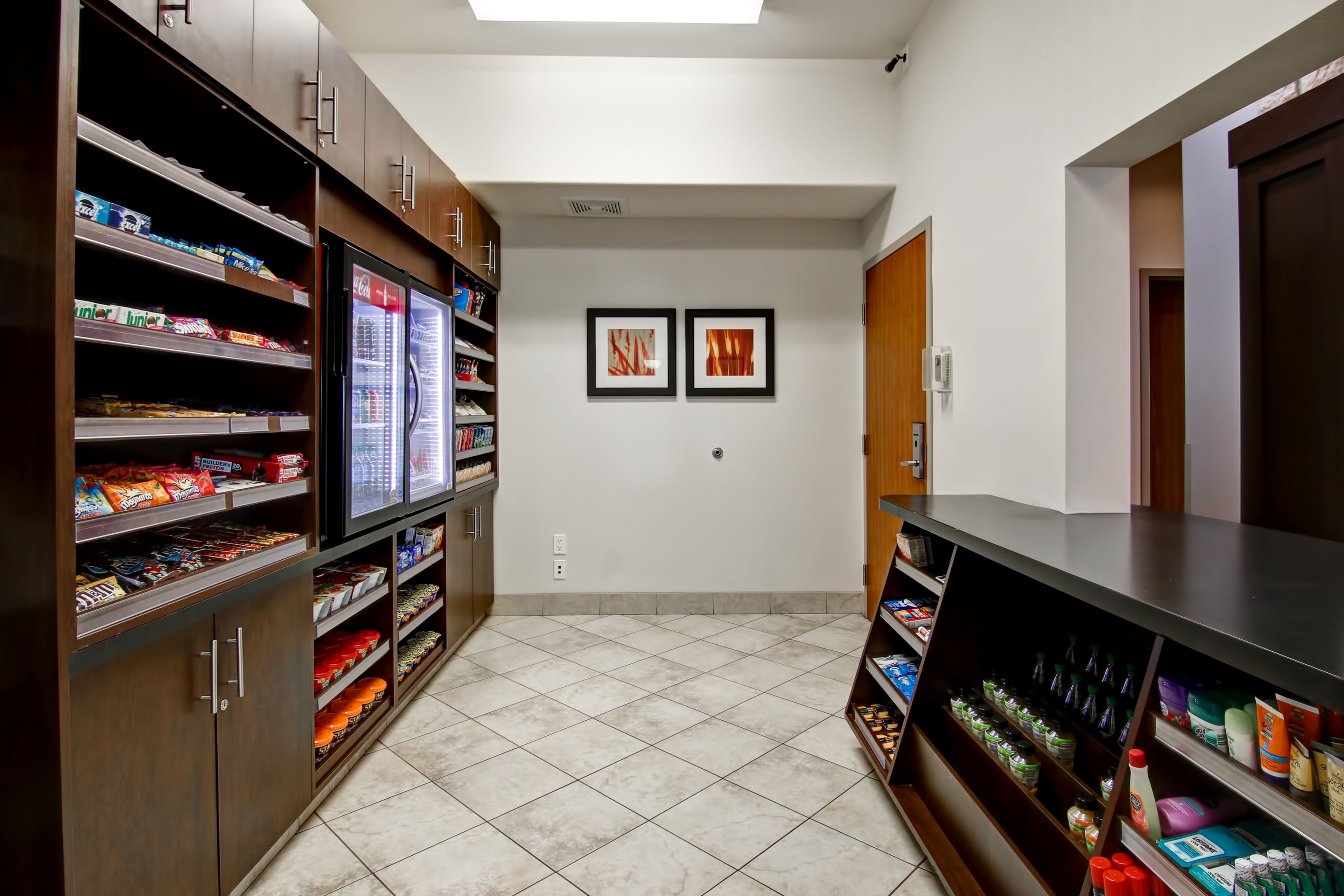 A hallway with snack shelves on both sides, a refrigerator, and two framed pictures on the wall.
