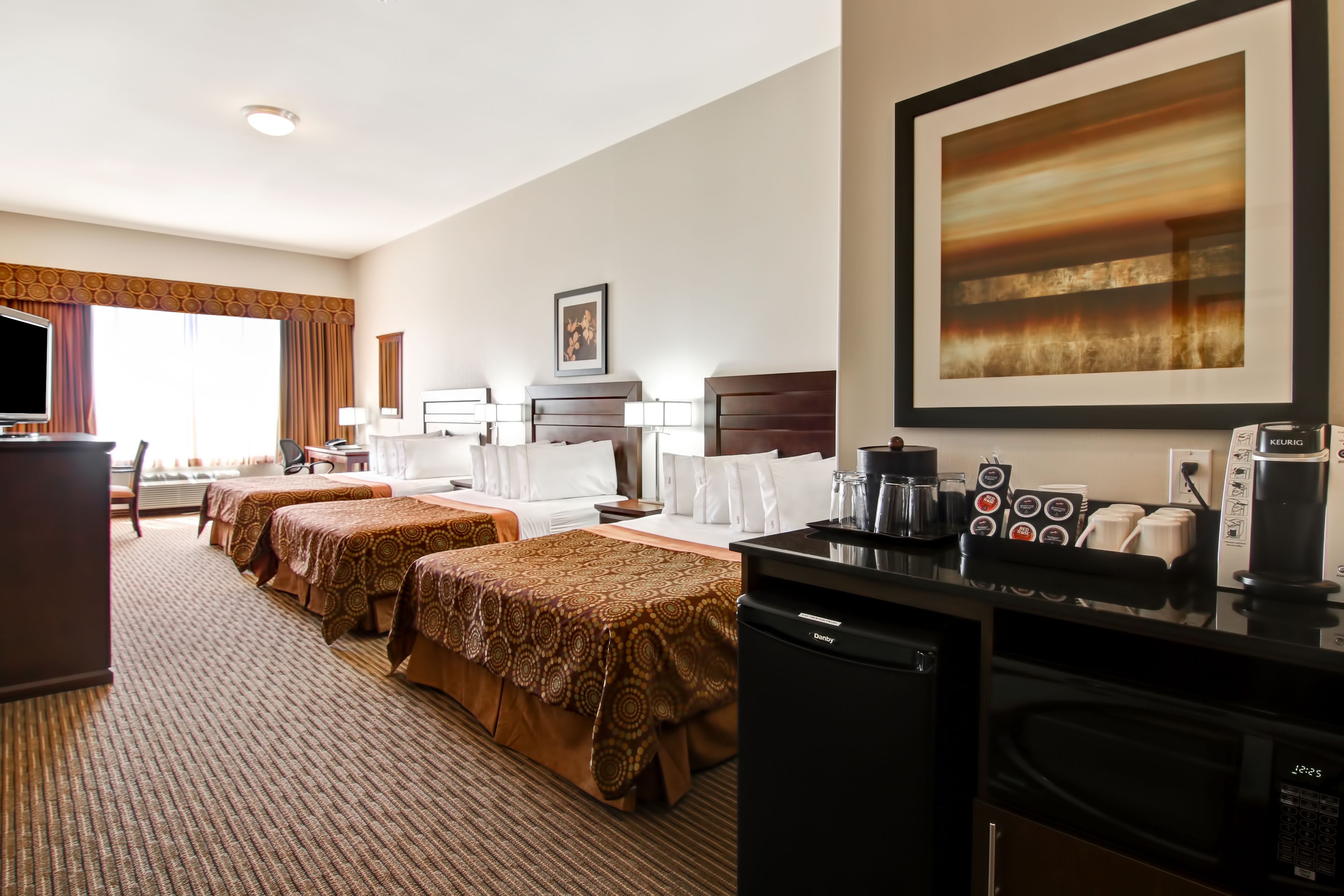 A hotel room with two beds, a desk, a television, a coffee maker, and a microwave.