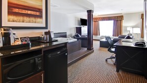 Ett hotellrum med ett litet kök, en platt-TV, en soffa, ett skrivbord och ett stort fönster med gardiner.