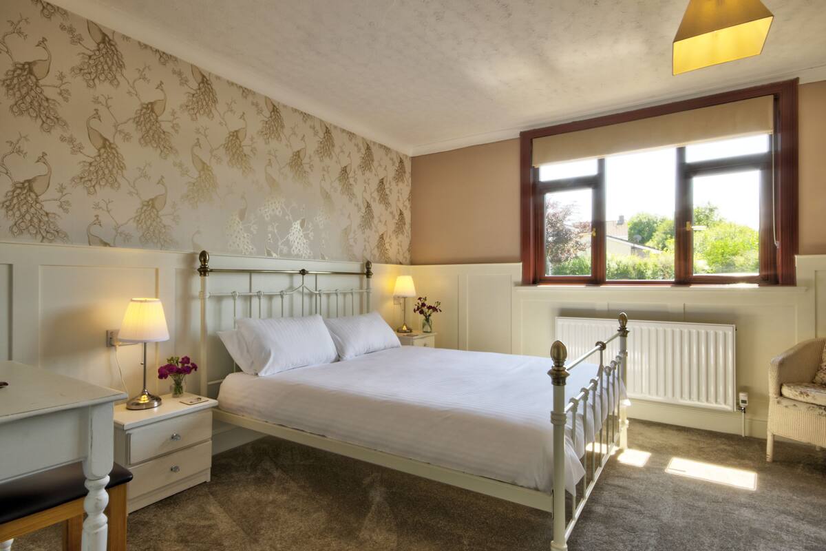 A bedroom with a bed, nightstands, a lamp, a window, and a radiator.