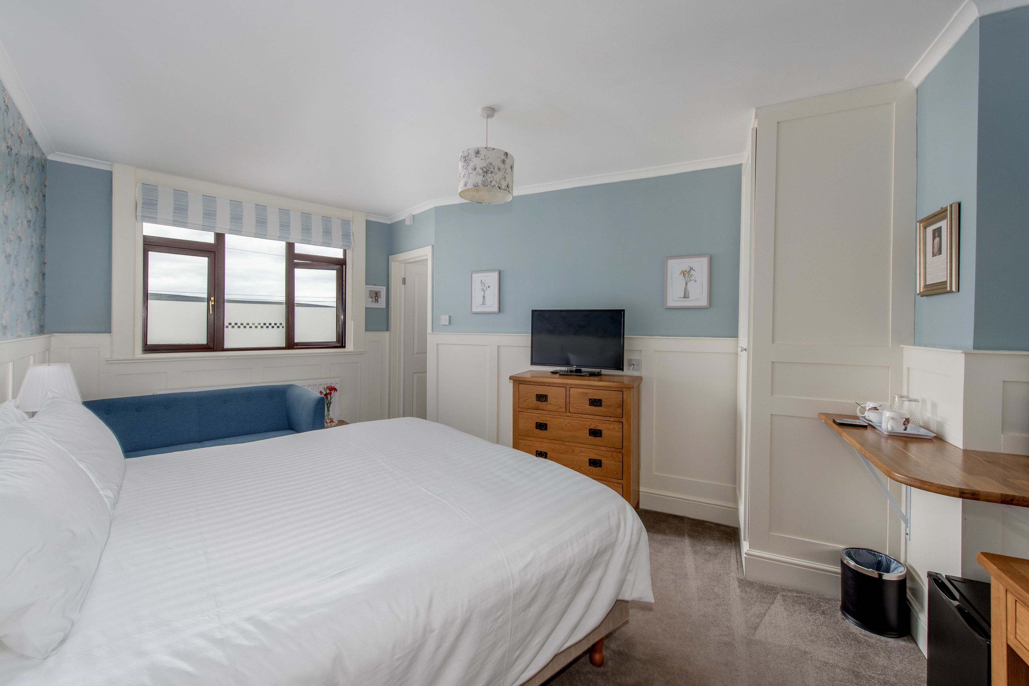 A bedroom with a large bed, a wooden dresser, a television, and a small table with a lamp.