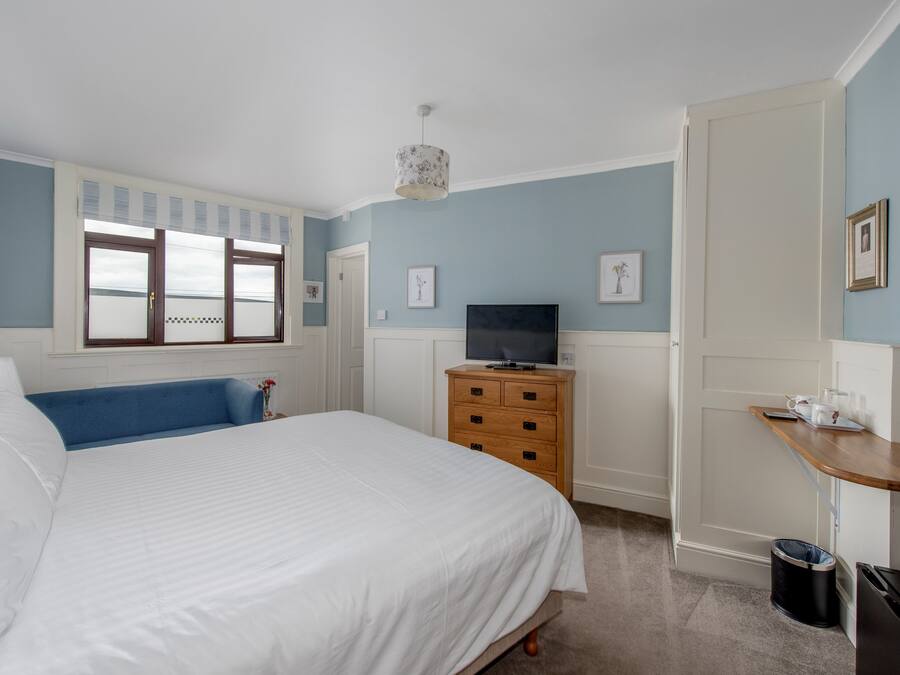 A bedroom with a large bed, a wooden dresser, a television, and a small table with a lamp.