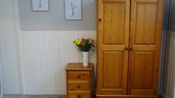A wooden wardrobe with two doors, a small wooden nightstand with drawers, and a vase with flowers on the nightstand.