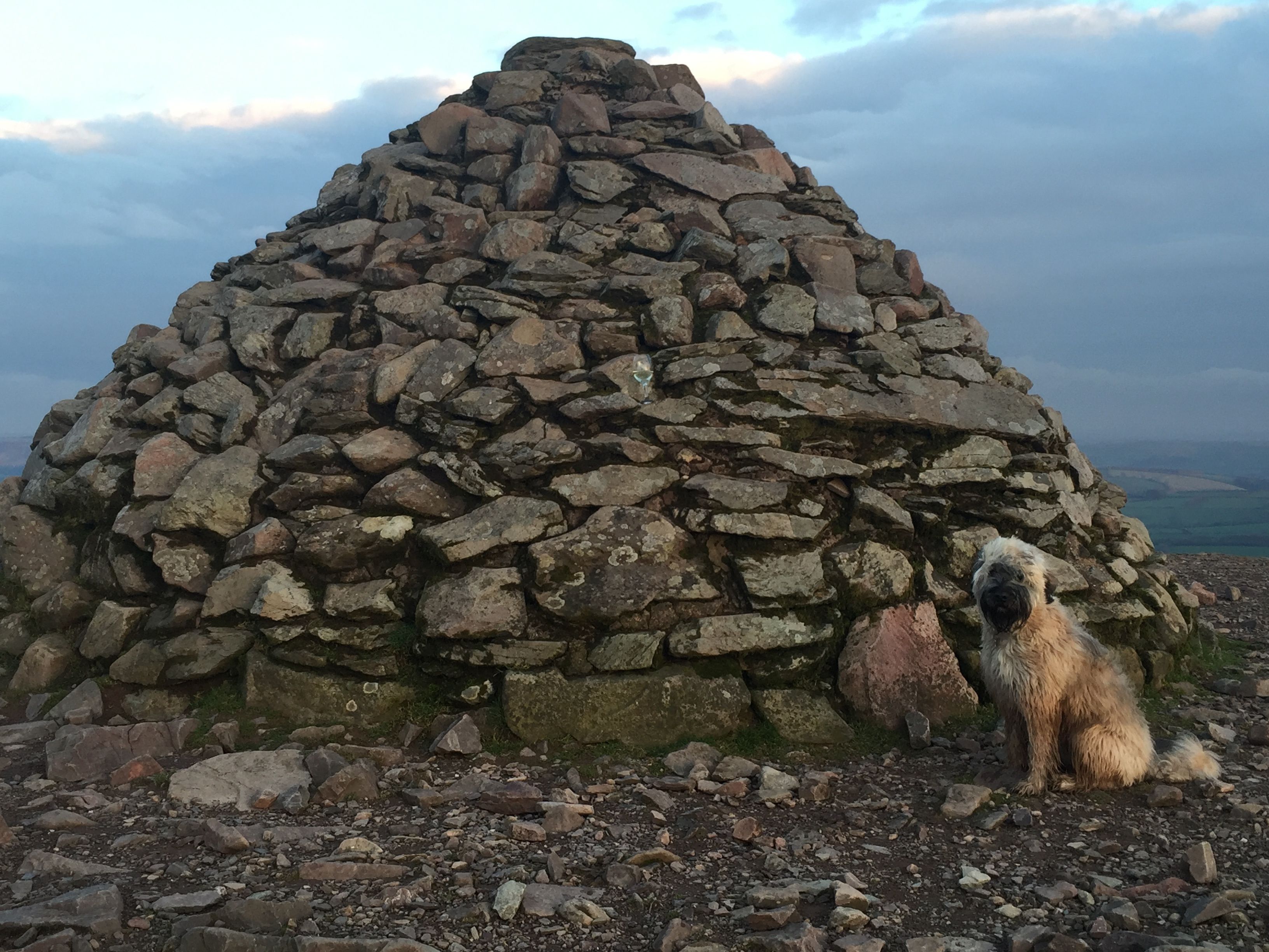 A stone cairn with a dog sitting in front of it.