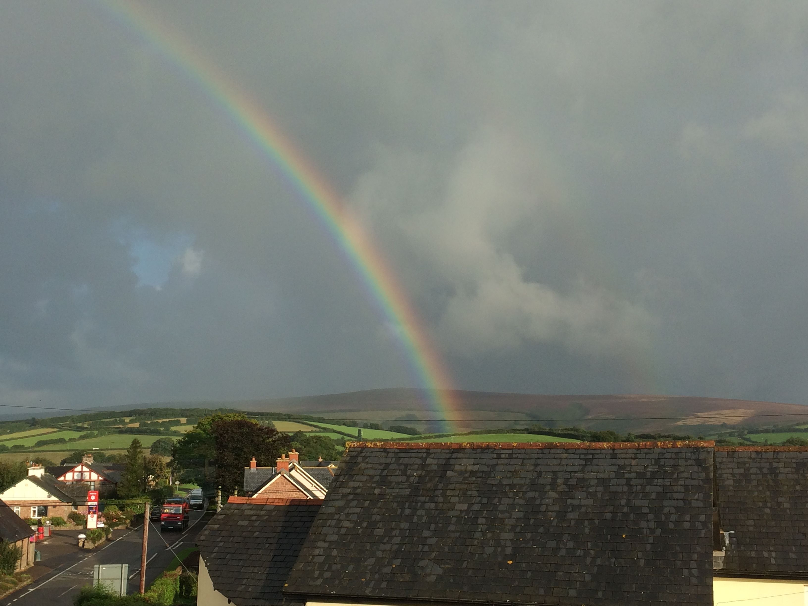 A rural landscape with a rainbow, houses, and a road.