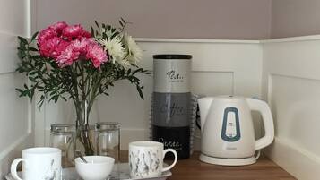 A kitchen counter with a tea kettle, a coffee maker, a mug, a bowl, and a tray with a vase of flowers.
