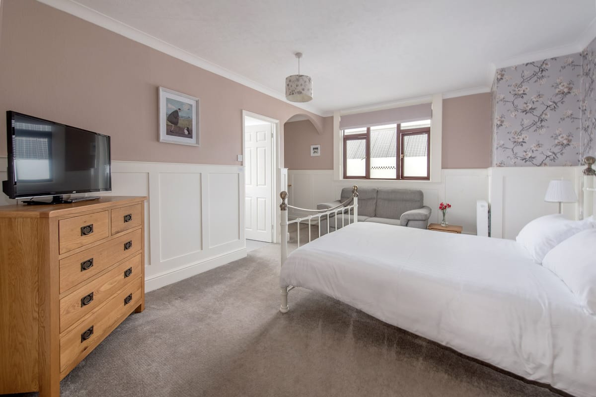 A bedroom with a bed, a dresser, a television, a window, and a door.
