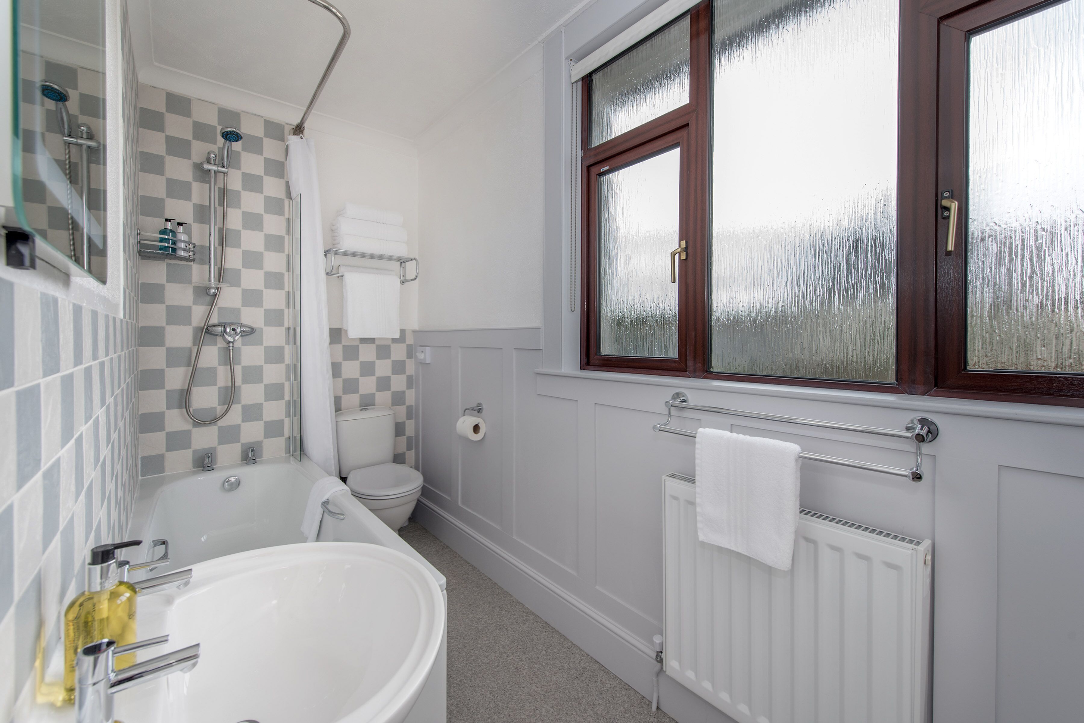 A bathroom with a bathtub, toilet, and a window with frosted glass.