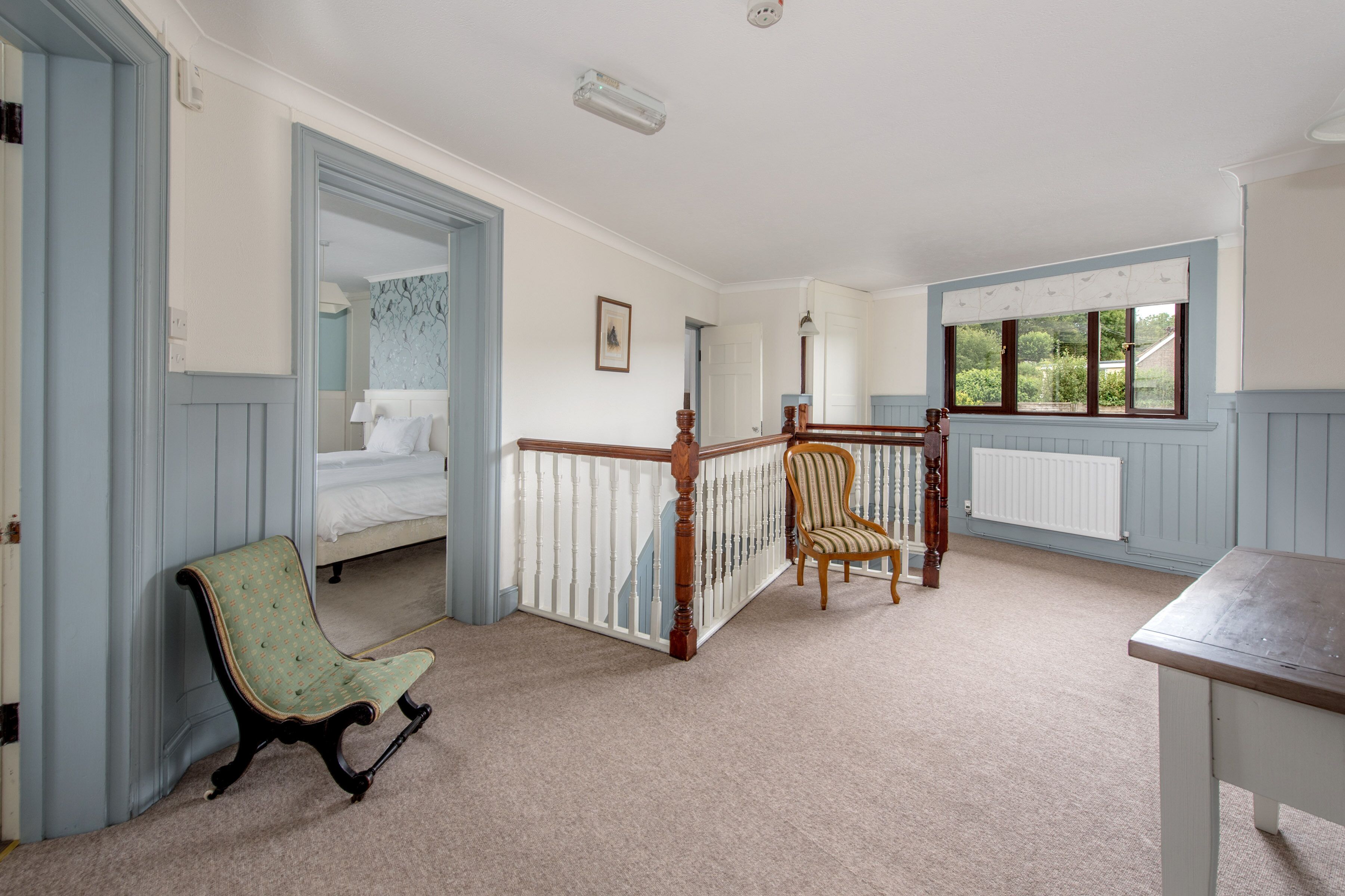 A room with a bed, a chair, a table, and a window with a view of greenery.