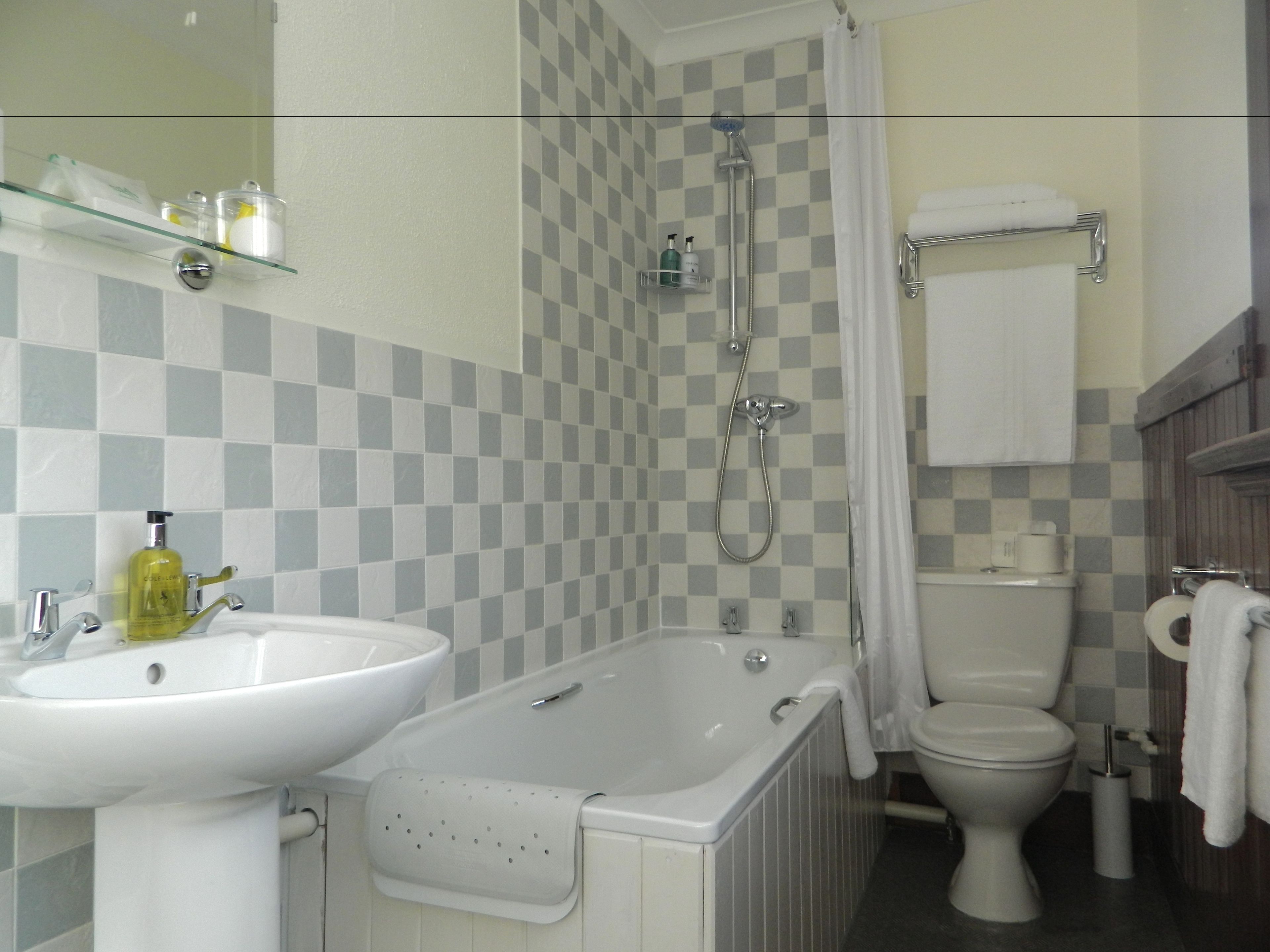 Un baño con pared de baldosas a cuadros, lavamanos, bañera, ducha e inodoro.