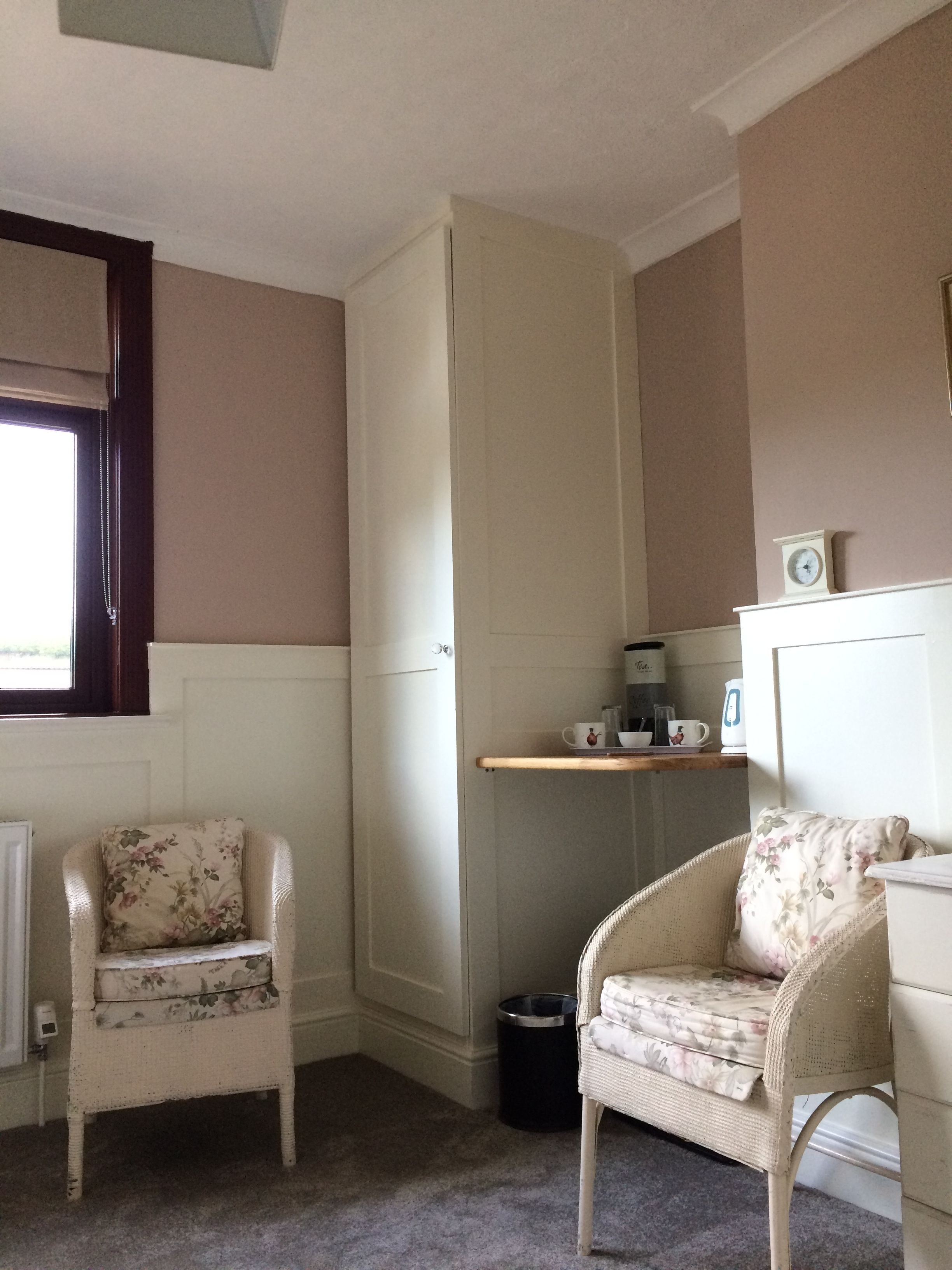 A small, cozy room with two wicker chairs, a white cabinet, and a window with a dark frame.