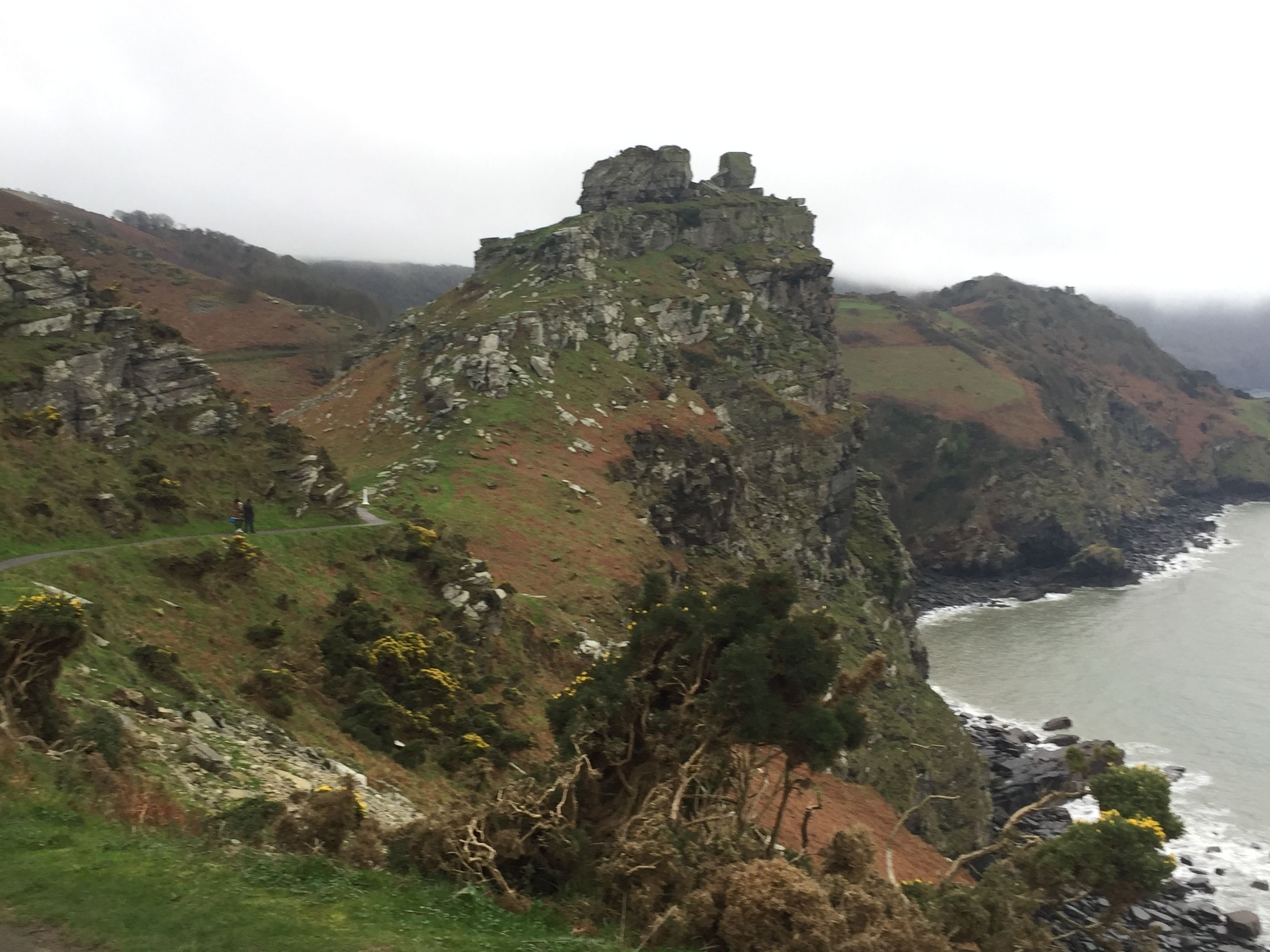A rugged coastal landscape with a prominent rocky cliff and a small structure on top.