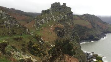 A rugged coastal landscape with a prominent rocky cliff and a small structure on top.