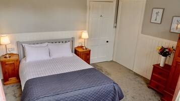 A bedroom with a bed, two bedside tables with lamps, a door, a dresser, and a wall with framed pictures.