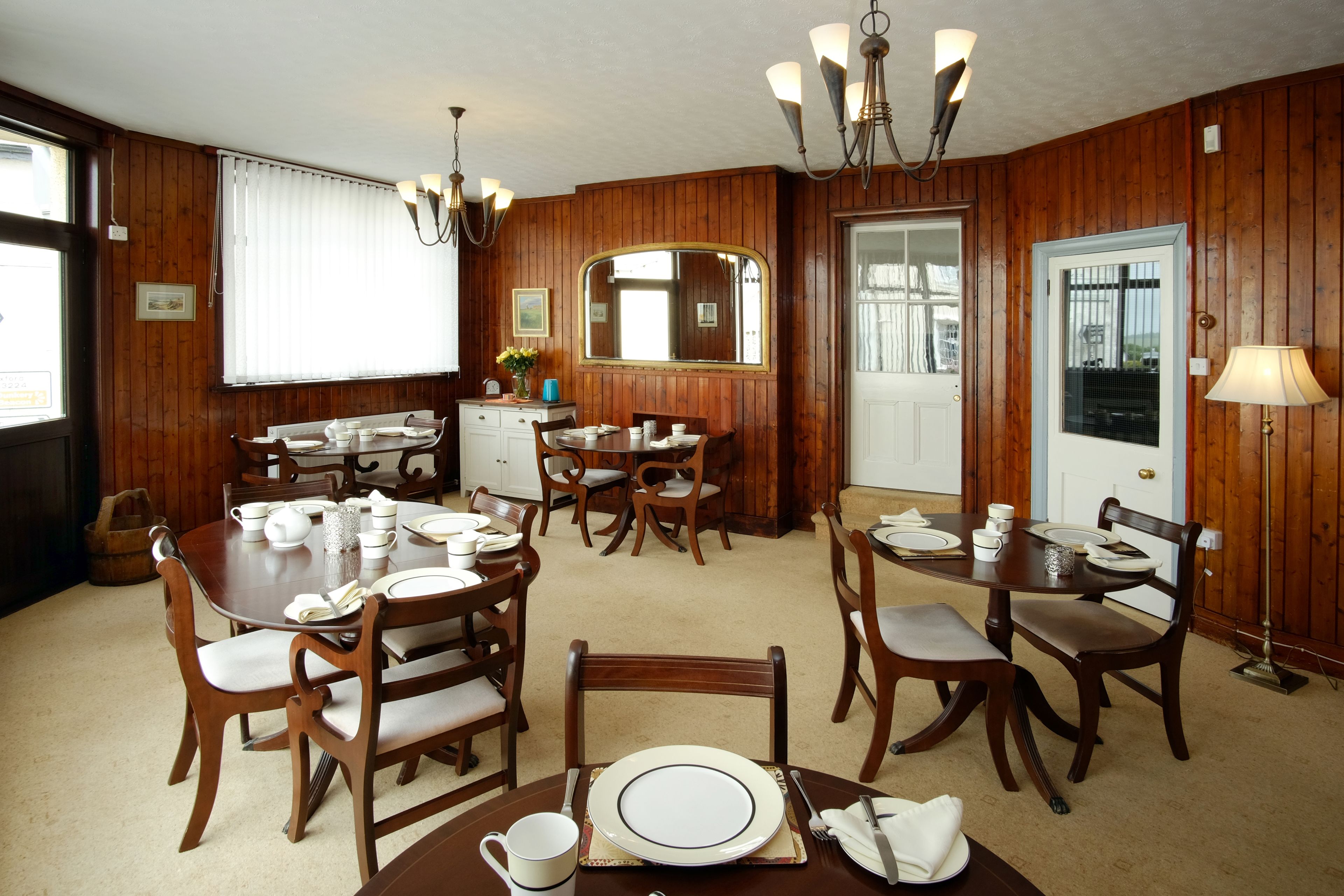 A dining room with wooden paneling, a chandelier, and a large mirror.