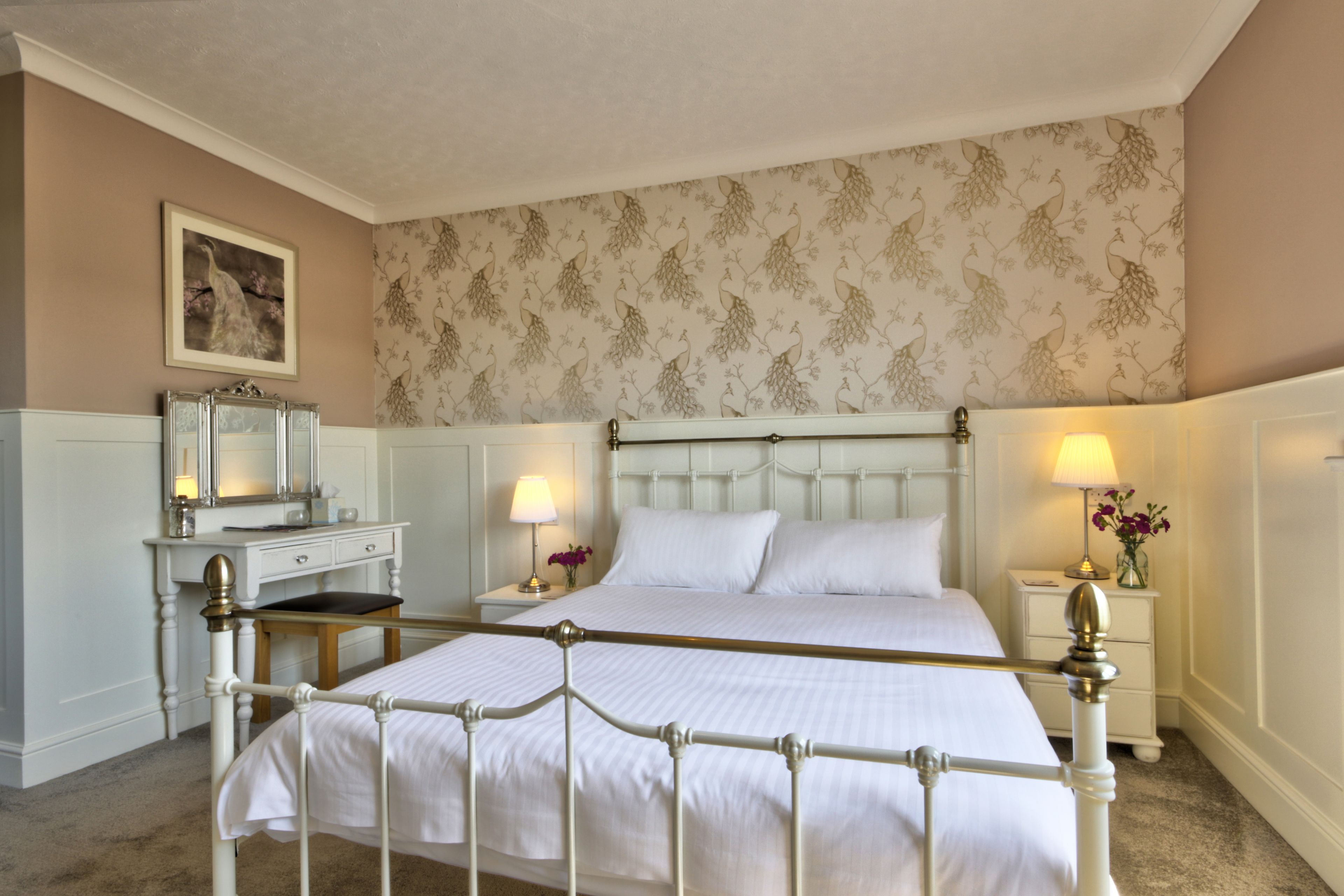 A neatly arranged bedroom with a large bed, a bedside table with a lamp, and a dresser.
