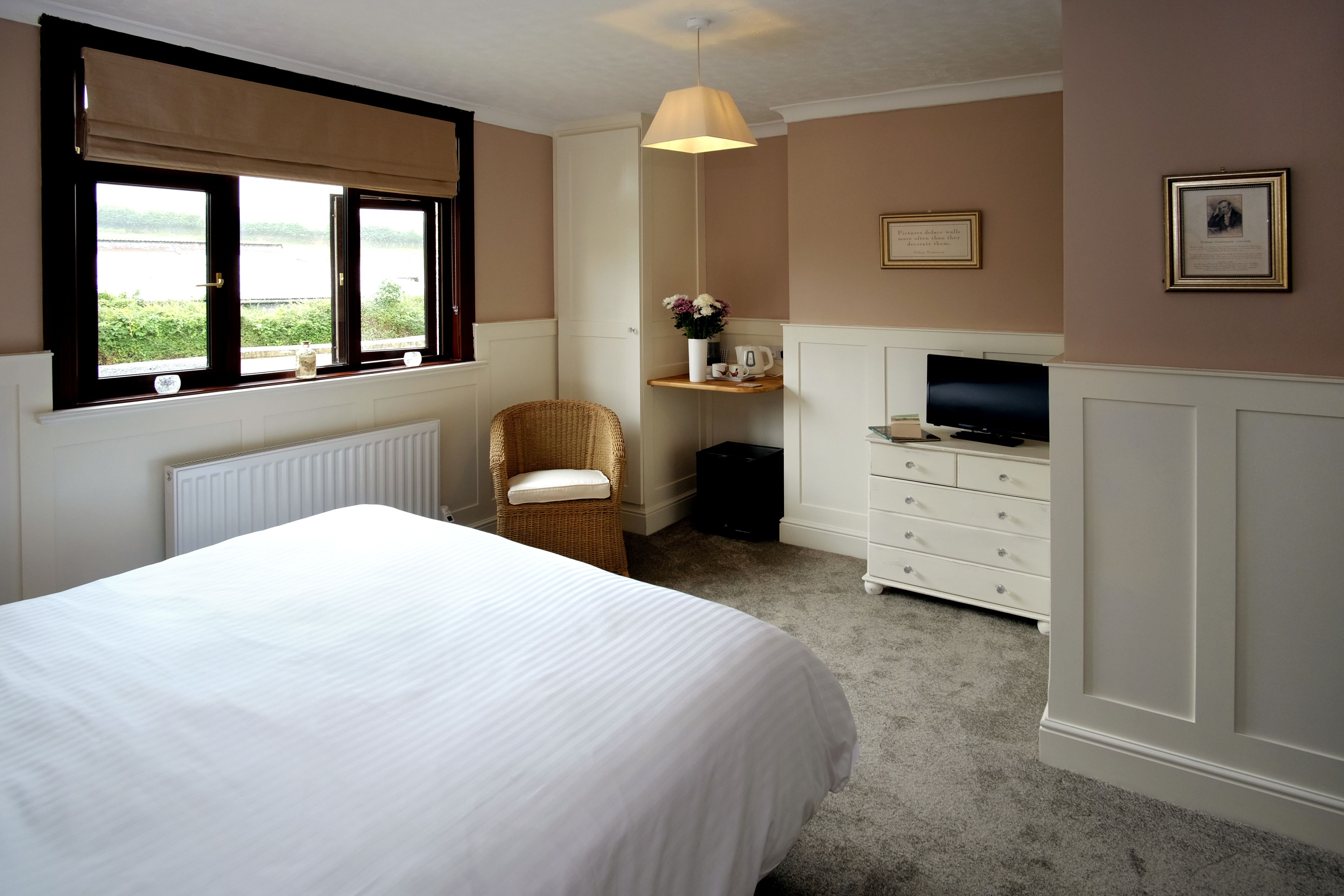 A bedroom with a bed, a chair, a TV, a dresser, and a shelf with flowers.