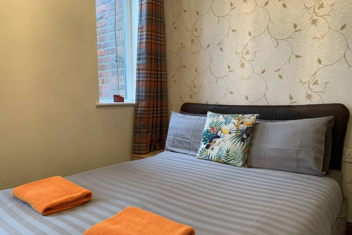 A hotel room with a bed, two pillows, a window with curtains, and a towel on the bed.