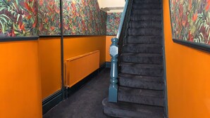 En trappa med ett svart räcke och en blå baluster, omgiven av orange väggar och en blommig tapet.