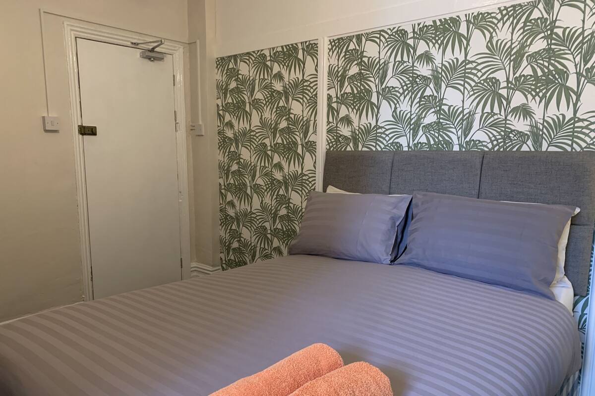 A neatly made bed with a striped bedspread, two pillows, and two rolled towels on the bed.
