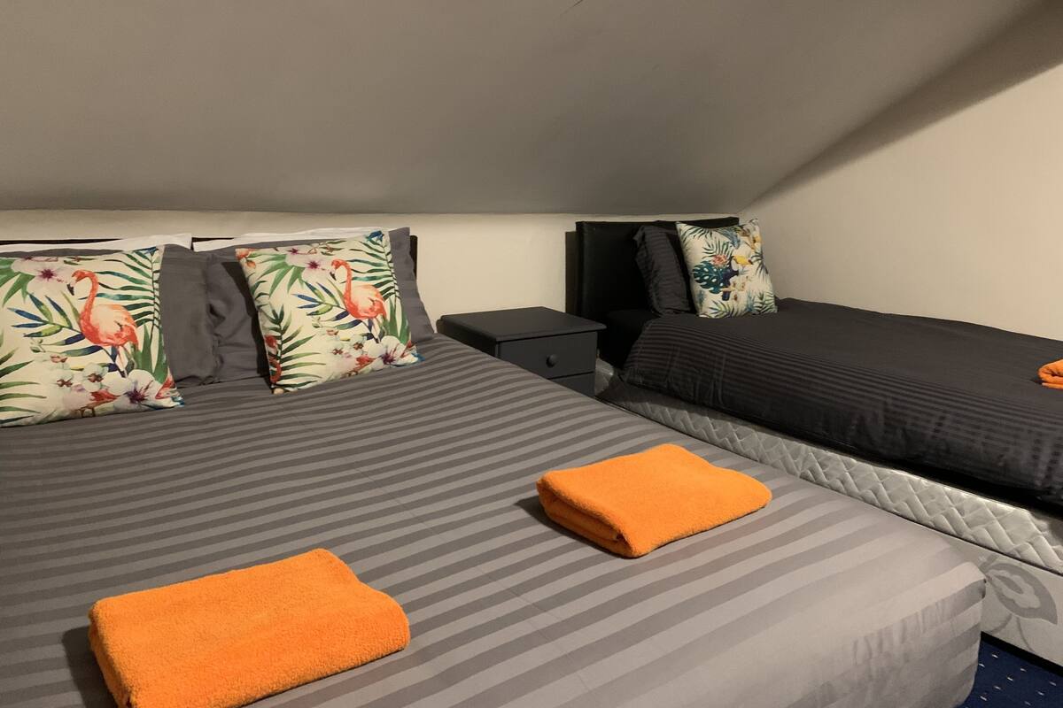 A hotel room with two beds, each with striped bedding and floral pillows. There is a nightstand and a folded orange towel on the floor.