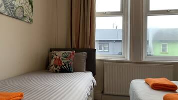A bedroom with two beds, a radiator, and a window with a view of buildings.